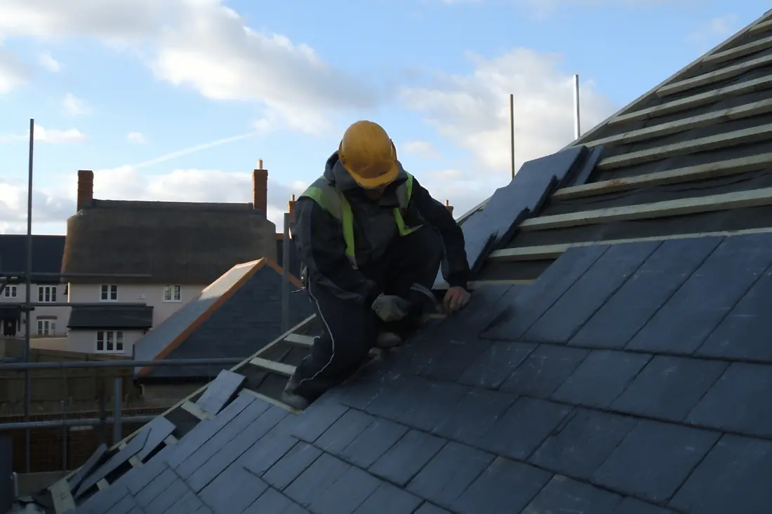 Roofer installing natural slate tiles on a steep roof